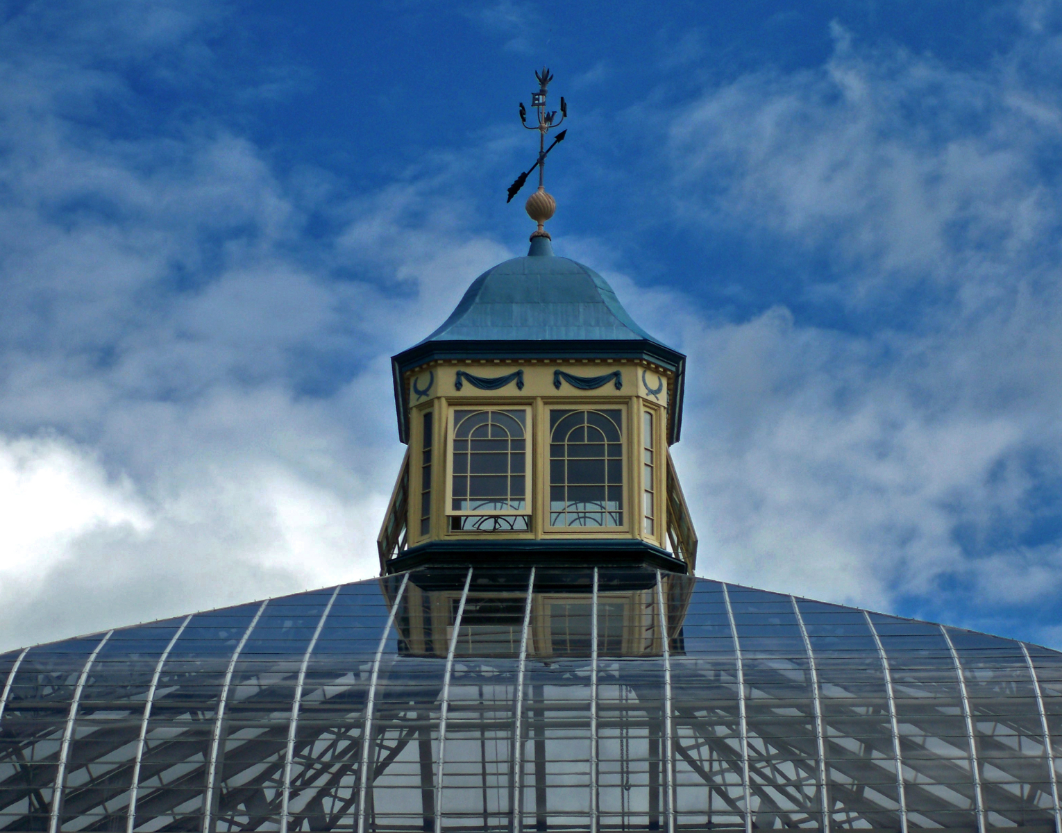 Palm House cupola and weathervane on cloudy day with a rich blue sky